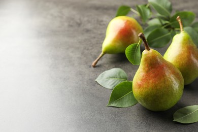 Photo of Fresh ripe pears and green leaves on grey table, closeup. Space for text