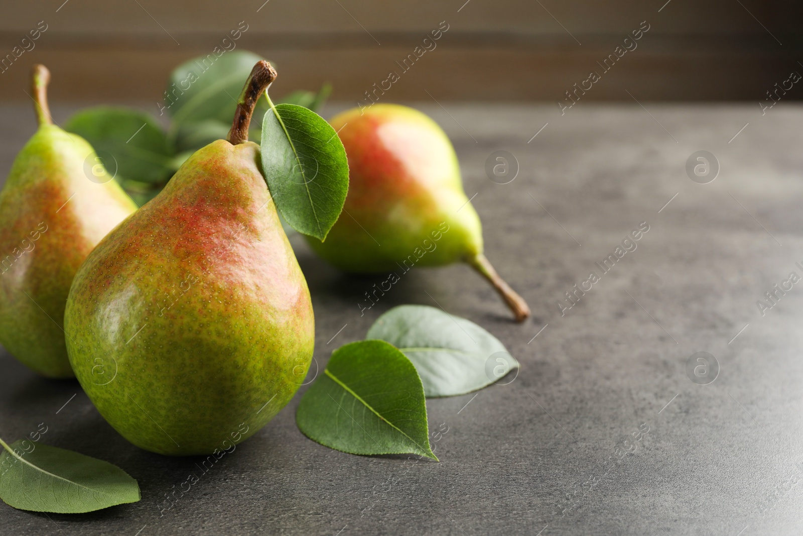 Photo of Fresh ripe pears and green leaves on grey table, closeup. Space for text