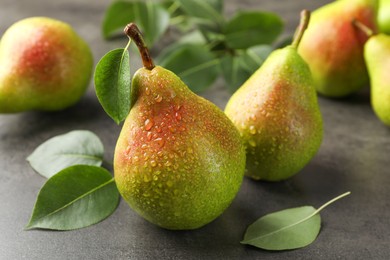 Photo of Fresh ripe pears and green leaves on grey table, closeup