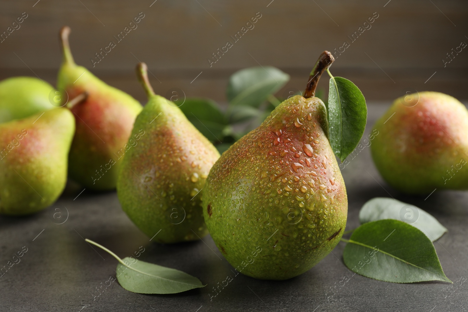 Photo of Fresh ripe pears and green leaves on grey table, closeup