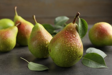 Photo of Fresh ripe pears and green leaves on grey table, closeup