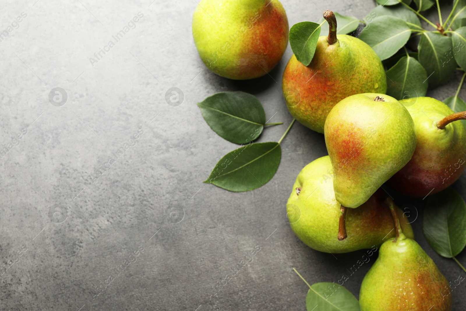 Photo of Fresh ripe pears and green leaves on grey table, flat lay. Space for text