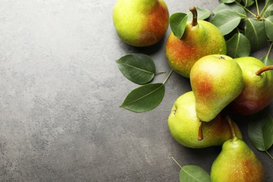 Photo of Fresh ripe pears and green leaves on grey table, flat lay. Space for text