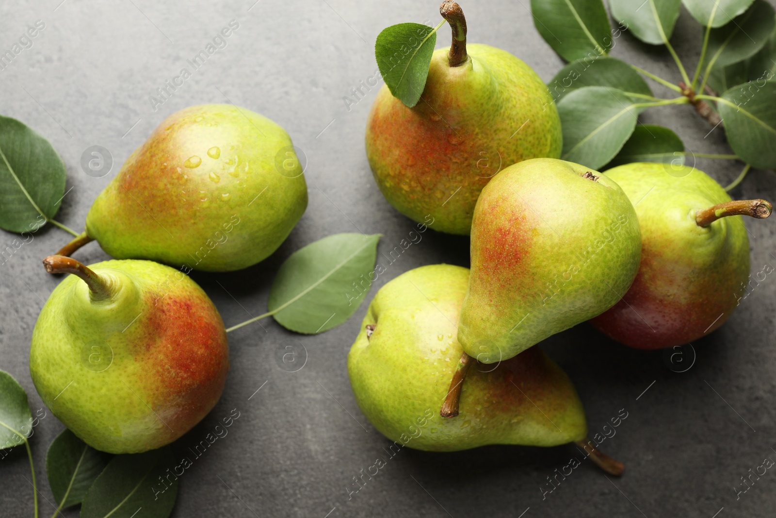 Photo of Fresh ripe pears and green leaves on grey table, flat lay
