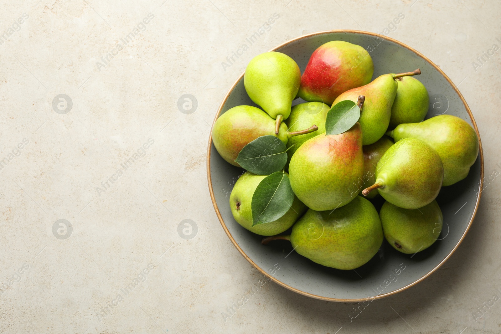 Photo of Fresh ripe pears and green leaves on light grey table, top view. Space for text
