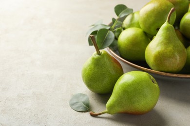 Photo of Fresh ripe pears and green leaves on light grey table, closeup. Space for text