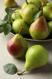 Photo of Fresh ripe pears and green leaves on light grey table, closeup