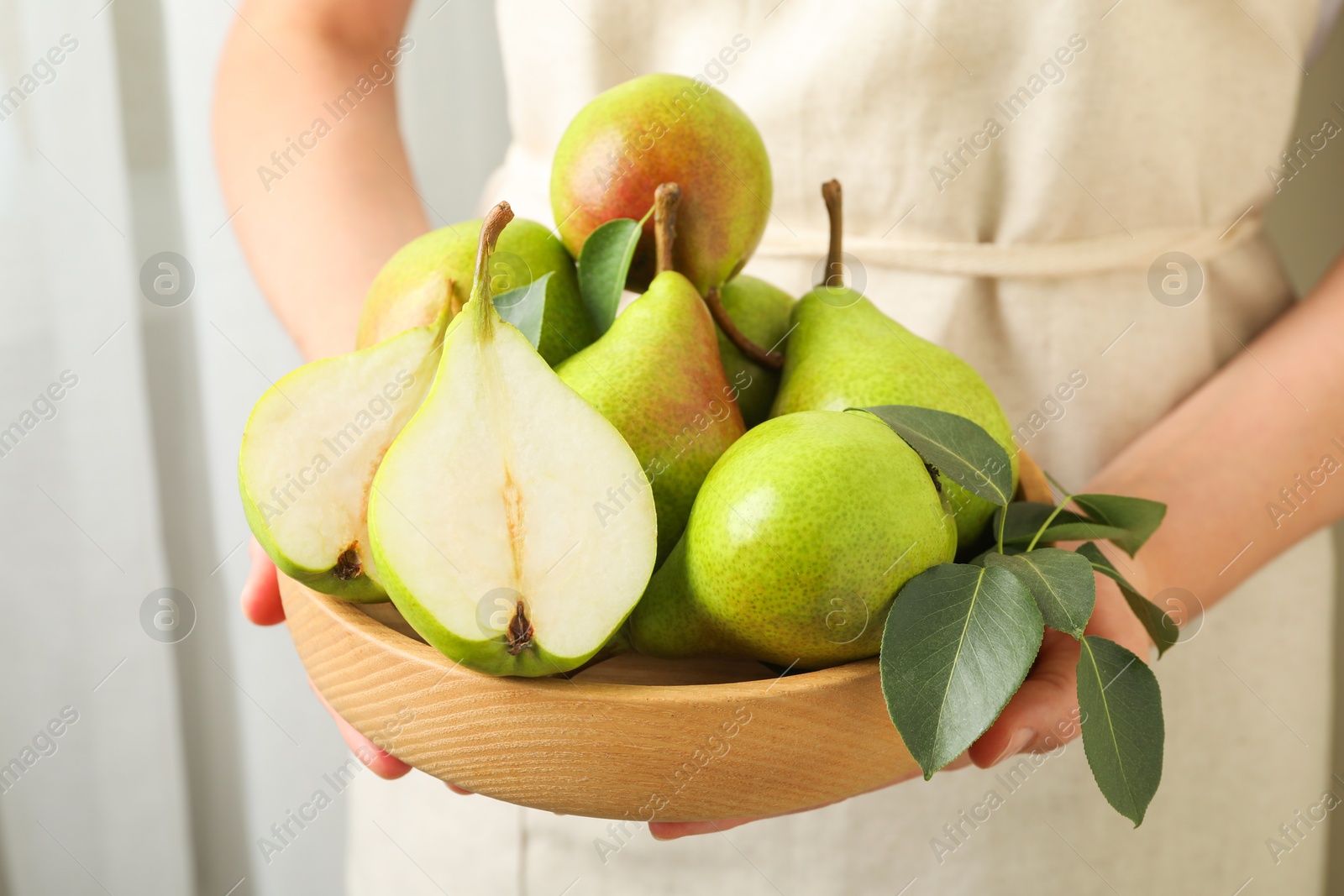 Photo of Woman with fresh ripe pears and green leaves indoors, closeup