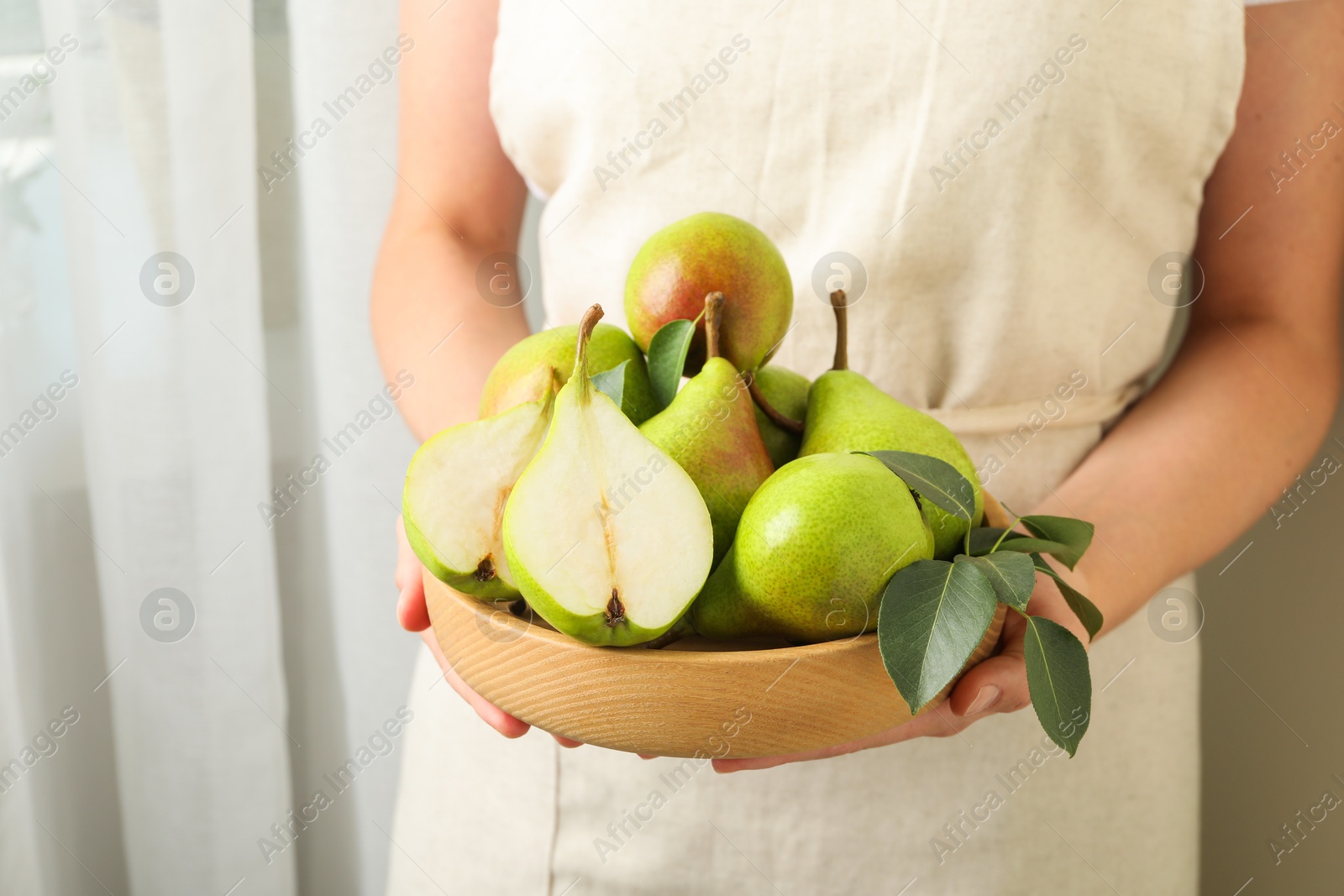 Photo of Woman with fresh ripe pears and green leaves indoors, closeup