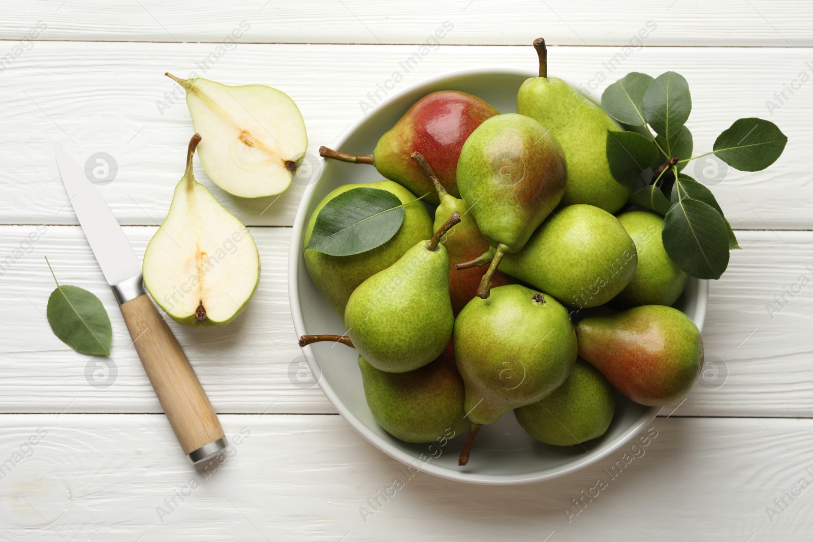 Photo of Fresh ripe pears, knife and green leaves on white wooden table, flat lay