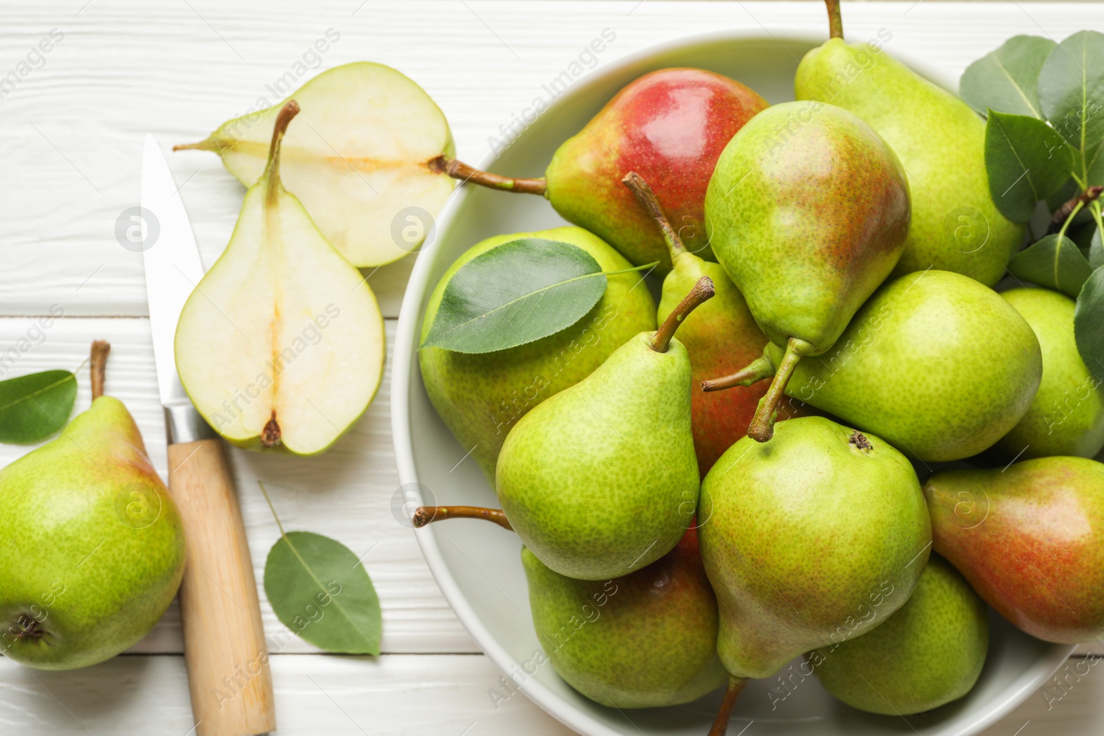 Photo of Fresh ripe pears, knife and green leaves on white wooden table, flat lay