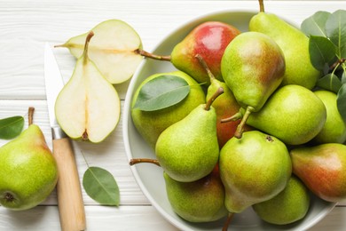 Photo of Fresh ripe pears, knife and green leaves on white wooden table, flat lay