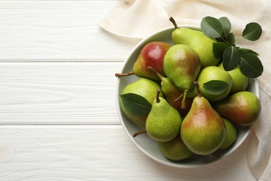 Photo of Fresh ripe pears in bowl and green leaves on white wooden table, top view. Space for text