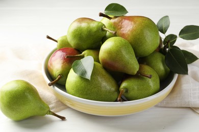 Photo of Fresh ripe pears in bowl and green leaves on white wooden table, closeup