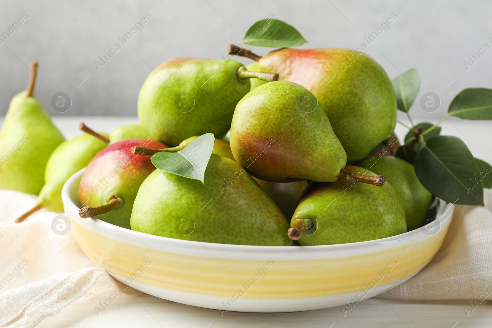 Fresh ripe pears in bowl and green leaves on white wooden table, closeup Photo of Fresh ripe pears in bowl and green leaves on white wooden table, closeup