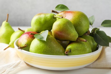 Photo of Fresh ripe pears in bowl and green leaves on white wooden table, closeup