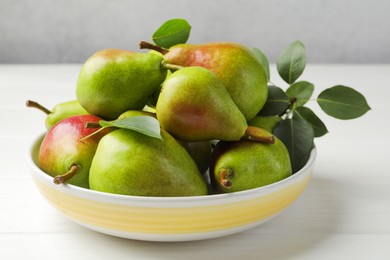 Photo of Fresh ripe pears in bowl and green leaves on white wooden table, closeup