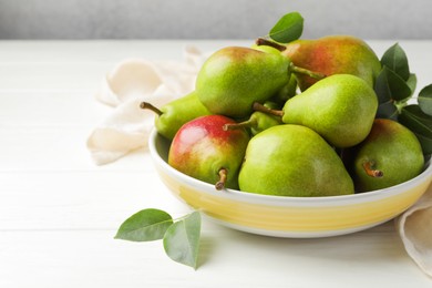 Photo of Fresh ripe pears in bowl and green leaves on white wooden table, closeup. Space for text