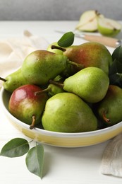Photo of Fresh ripe pears in bowl and green leaves on white wooden table, closeup