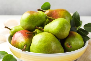 Photo of Fresh ripe pears in bowl and green leaves on table, closeup
