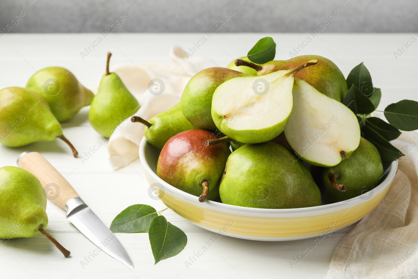 Photo of Fresh ripe pears, knife and green leaves on white wooden table, closeup