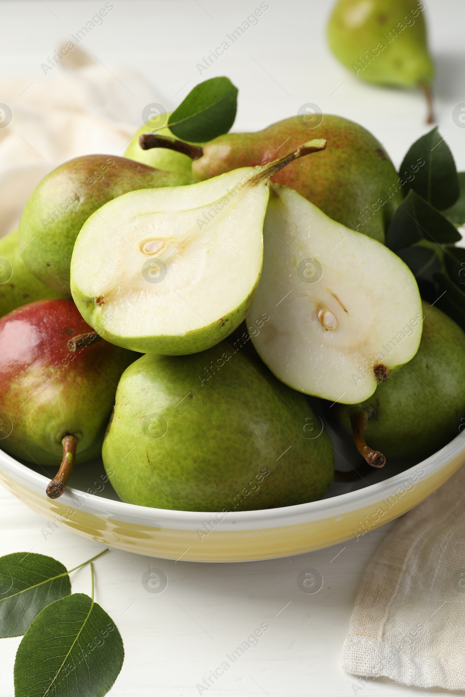 Fresh ripe pears in bowl and green leaves on white wooden table, closeup Photo of Fresh ripe pears in bowl and green leaves on white wooden table, closeup