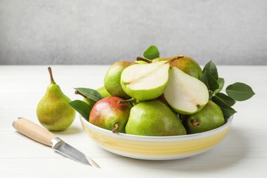 Photo of Fresh ripe pears, knife and green leaves on white wooden table, closeup