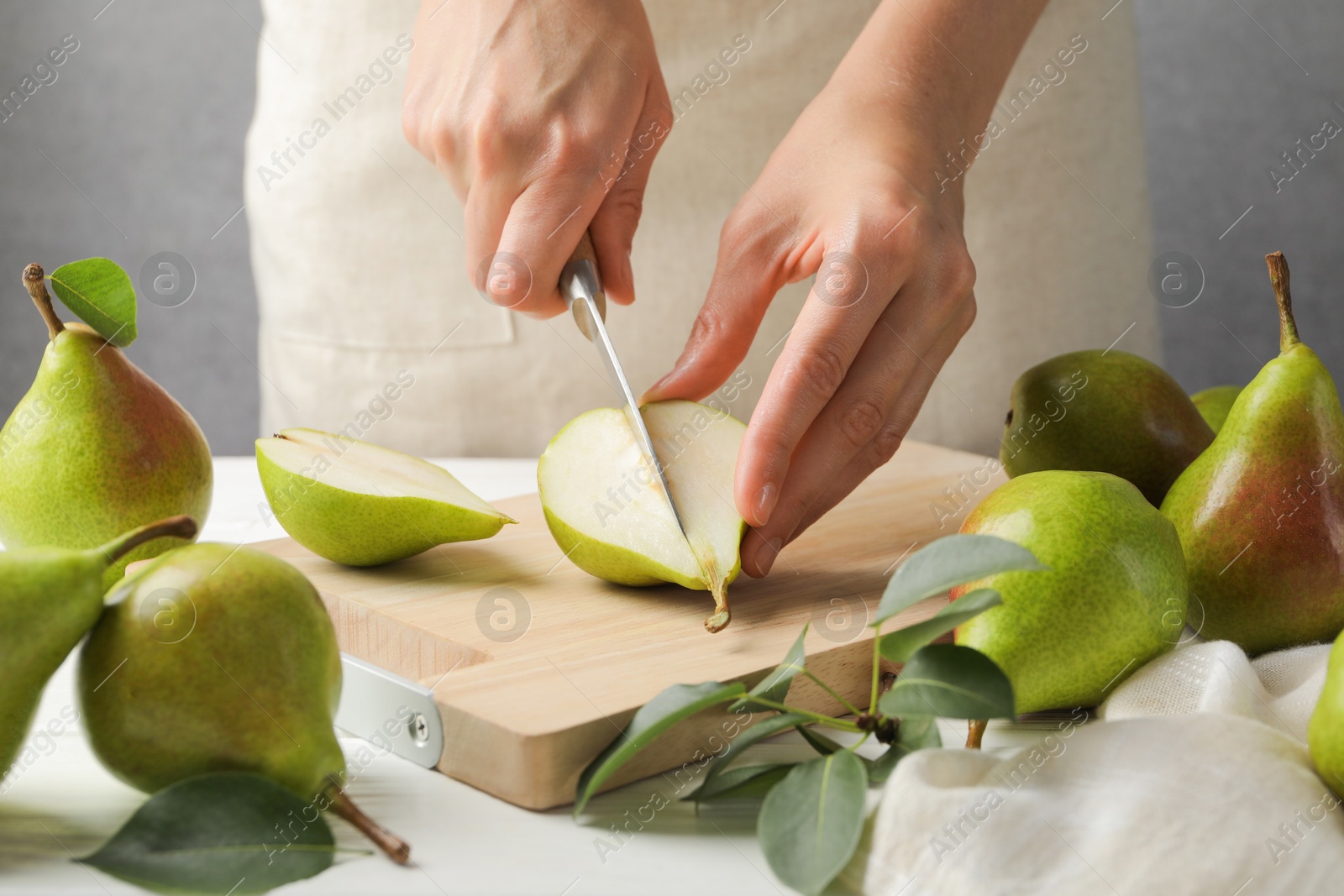 Photo of Woman cutting fresh ripe pear at white wooden table, closeup