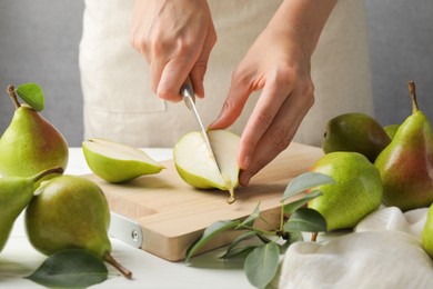 Photo of Woman cutting fresh ripe pear at white wooden table, closeup