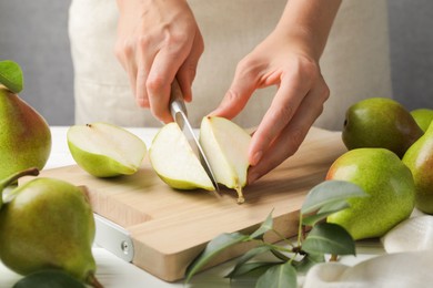 Photo of Woman cutting fresh ripe pear at white wooden table, closeup