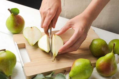 Photo of Woman cutting fresh ripe pear at white wooden table, closeup