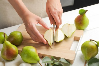 Photo of Woman cutting fresh ripe pear at white wooden table, closeup