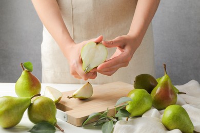 Photo of Woman cutting fresh ripe pear at white wooden table, closeup