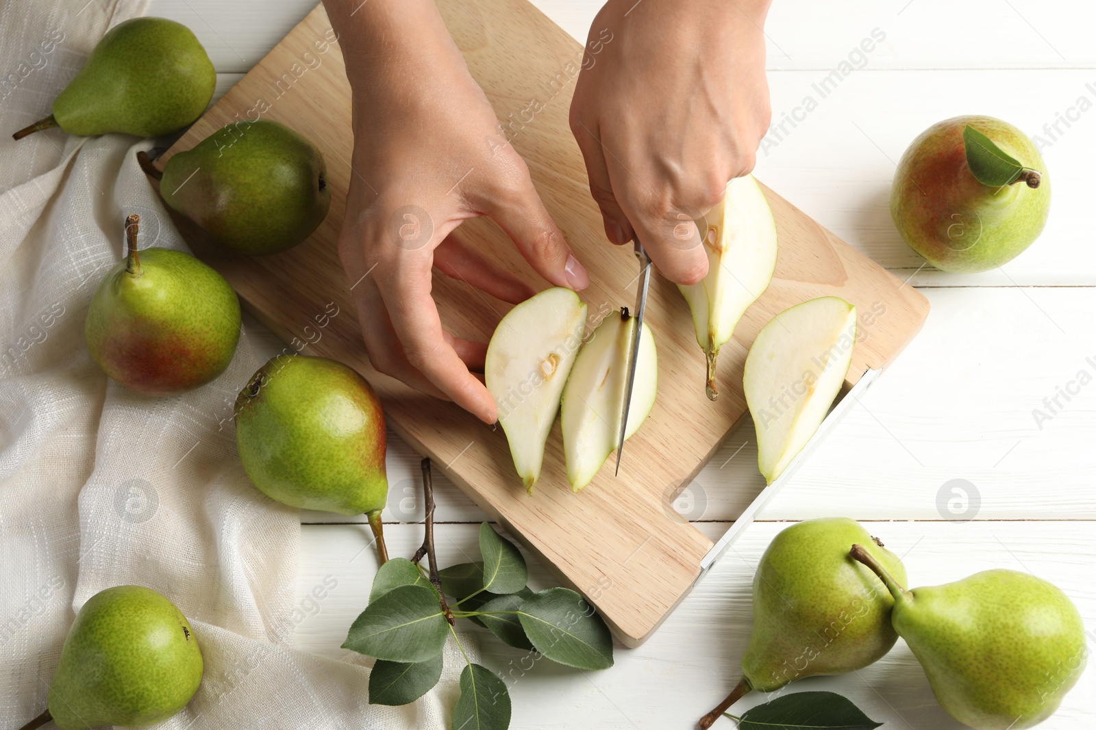 Photo of Woman cutting fresh ripe pear at white wooden table, top view