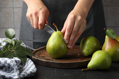 Photo of Woman cutting fresh ripe pear at black table, closeup
