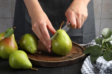 Photo of Woman cutting fresh ripe pear at black table, closeup