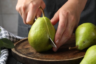 Photo of Woman cutting fresh ripe pear at table, closeup