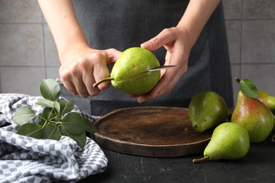 Photo of Woman cutting fresh ripe pear at black table, closeup