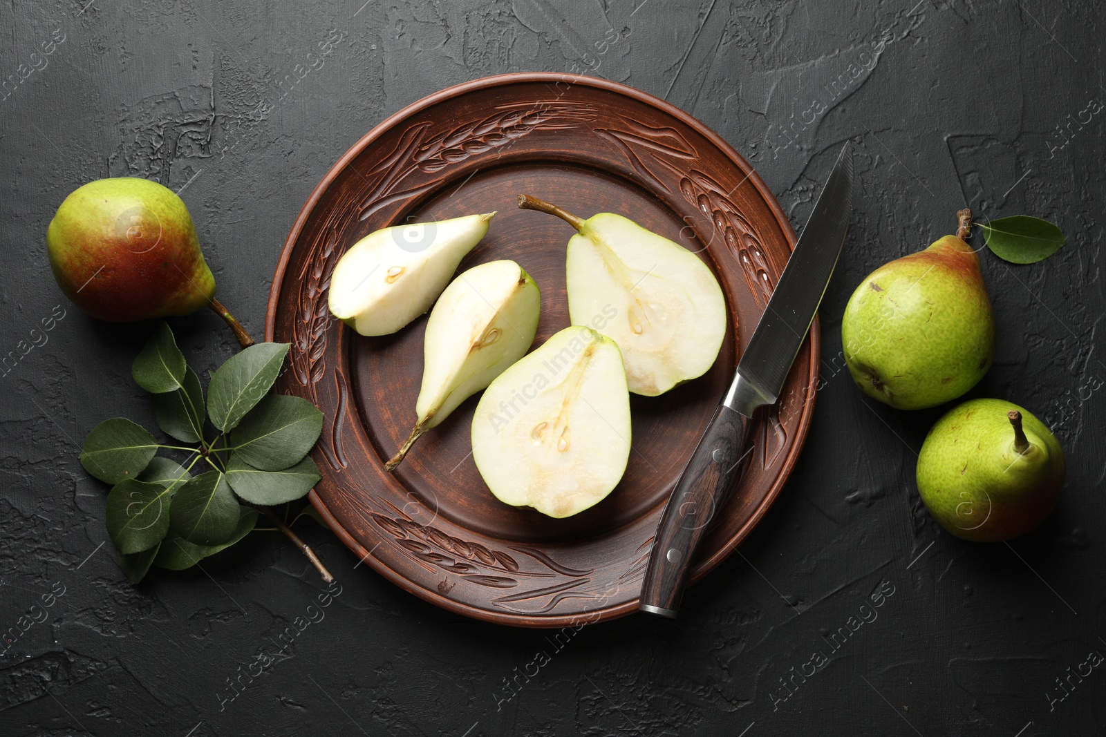 Photo of Fresh ripe pears, knife and green leaves on black table, flat lay