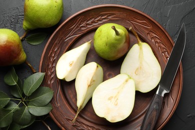 Photo of Fresh ripe pears, knife and green leaves on black table, flat lay