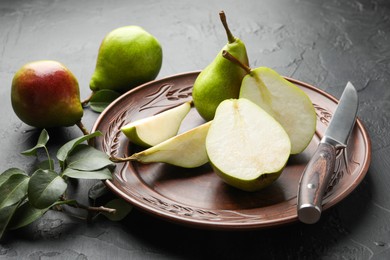 Photo of Fresh ripe pears, knife and green leaves on black table, closeup