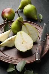 Photo of Fresh ripe pears, knife and green leaves on black table, closeup
