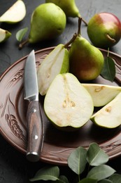Photo of Fresh ripe pears, knife and green leaves on black table, closeup