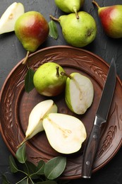 Photo of Fresh ripe pears, knife and green leaves on black table, flat lay