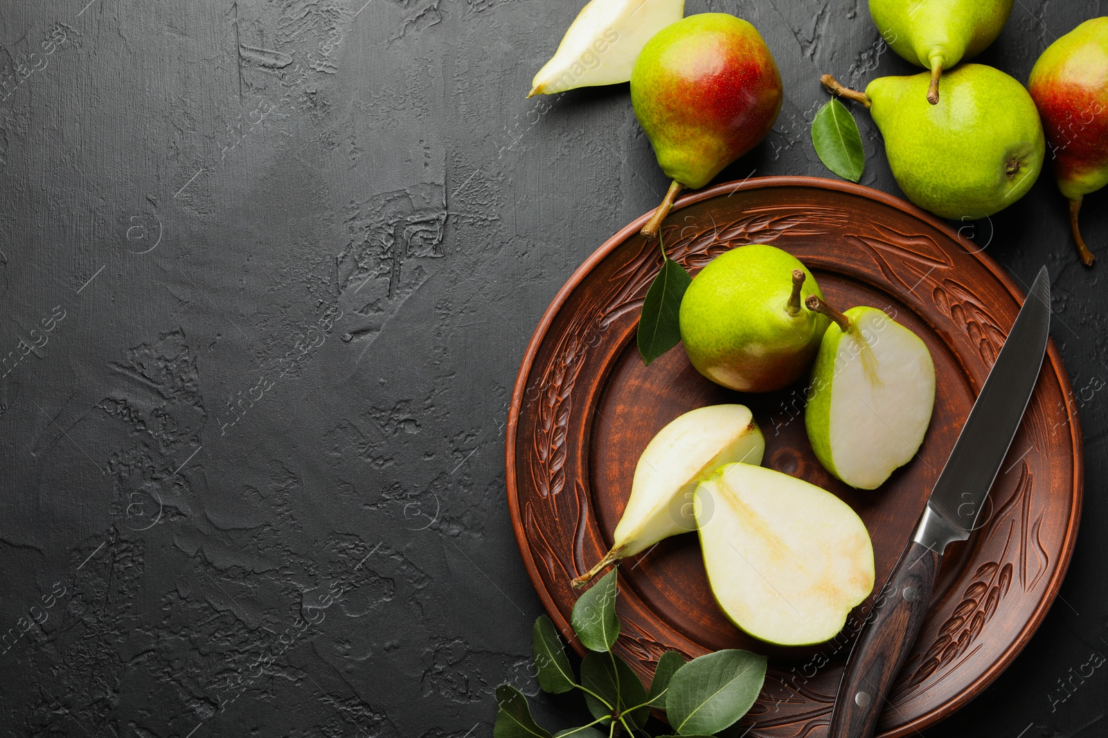 Photo of Fresh ripe pears, knife and green leaves on black table, flat lay. Space for text