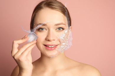 Image of Young woman with ice cube and water splashes on pink beige background