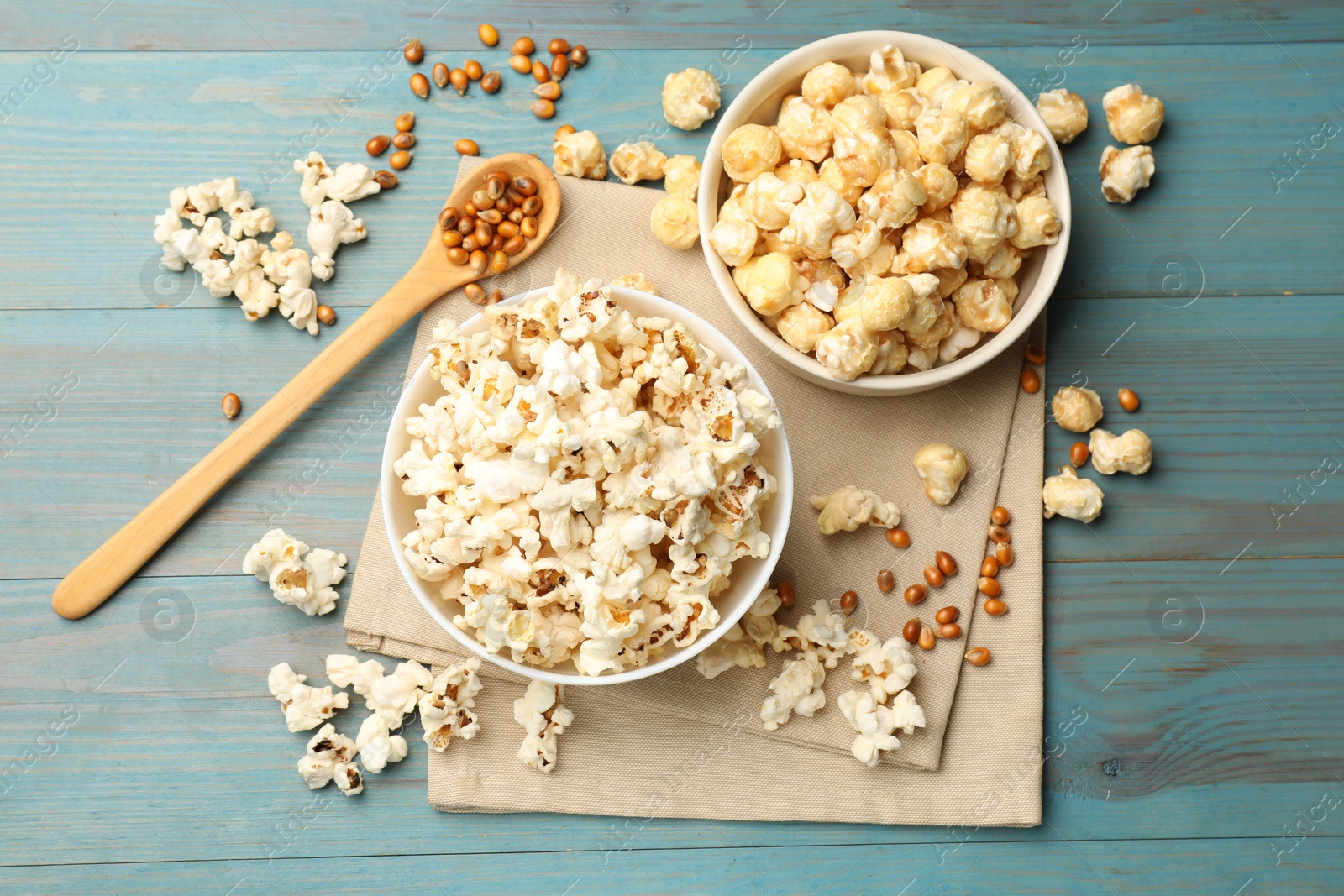 Photo of Tasty popcorn and corn kernels on light blue wooden table, flat lay