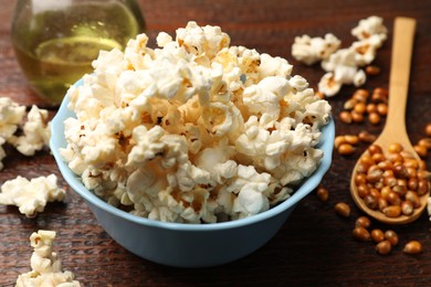 Photo of Tasty popcorn, oil and corn kernels on wooden table, closeup
