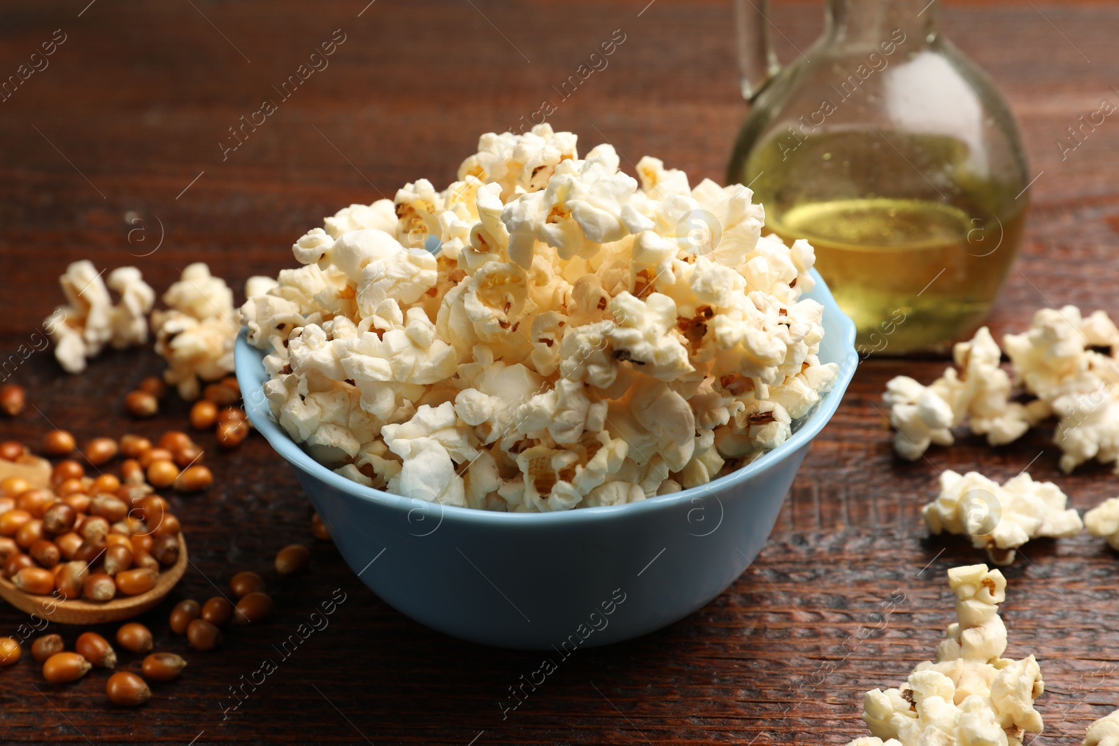 Photo of Tasty popcorn, oil and corn kernels on wooden table, closeup