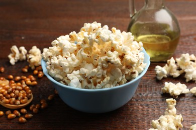 Photo of Tasty popcorn, oil and corn kernels on wooden table, closeup